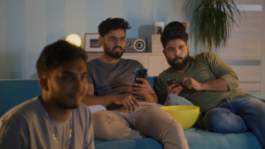 Indian friends watching cricket on tv while betting on their phones